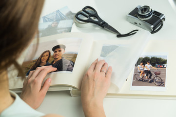 Looking at family wedding photo album. Young female engaged or married personturns pages and selects images for photoalbum