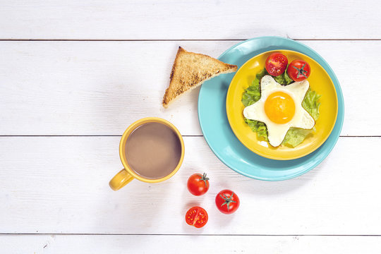Funny Breakfast with star-shaped fried egg, toast, cherry tomato, lettuce on colored plates and coffee.