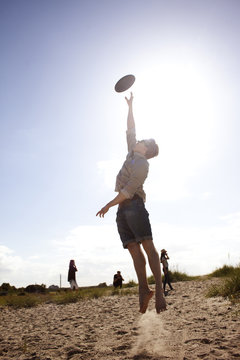 Full length of young man reaching for flying disc in air at beach