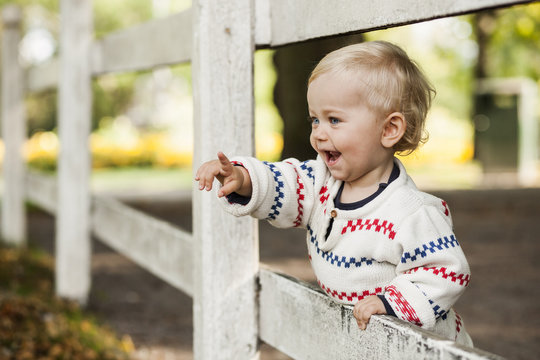 Smiling baby girl standing by wooden fence, pointing
