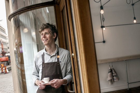 Smiling male barista holding coffee cup outside shop