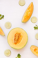 Cantaloupe melon half and slices and lime on white background. Top view, copy space, flat lay