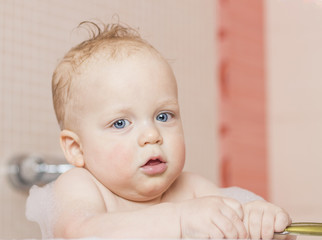 Close-up portrait of cute blue-eyed surprised baby boy in a bathtub.
