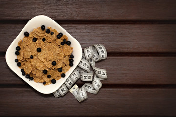  Corn flakes with berries in white plate on brown wooden boards. Nearby lies a meter. Background, texture, close-up. View from above