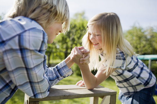Siblings arm wrestling on wooden table in back yard