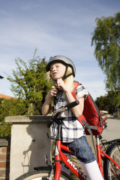 Girl fastening helmet while standing with bicycle on sunny day
