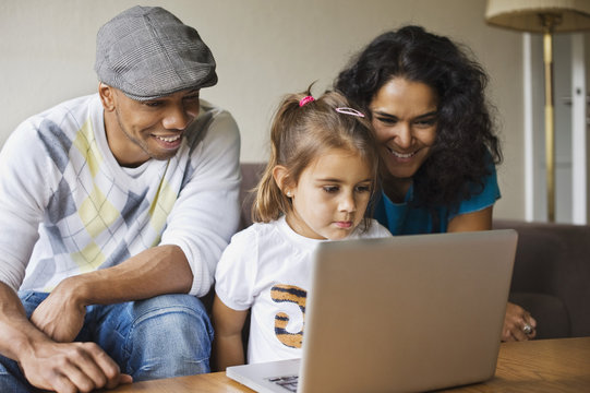 Happy father and mother with daughter using laptop at home