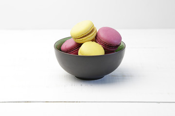 Brown bowl with yellow and pink macarons over an old white wooden table