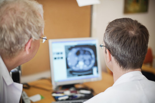 Rear view of doctors looking at radiogram image on desktop pc in hospital