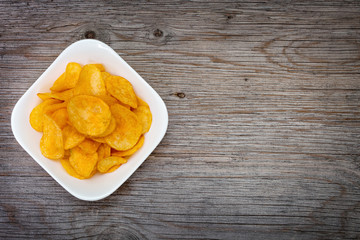 Salted potato chips in white bowl  on  gray wooden table. Close up. View from above. Space for text.
