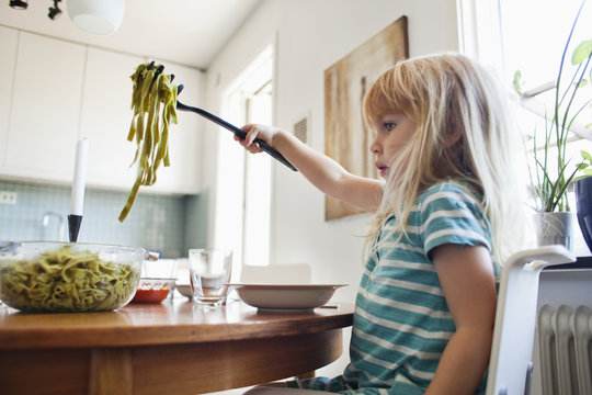 Side View Of Girl Holding Tagliatelle Pasta In Fork Over Bowl At Home