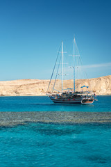 Fototapeta na wymiar Sail boat in the coral sea near island. Summer vacation in an exotic country. Red sea with clear turquoise water.