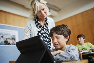 Low angle view of teacher assisting boy using digital tablet at classroom