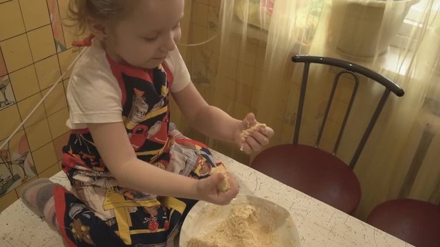 A small child sits on the table and knead the dough
