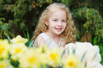 Happy little girl with her bear toy in blooming garden