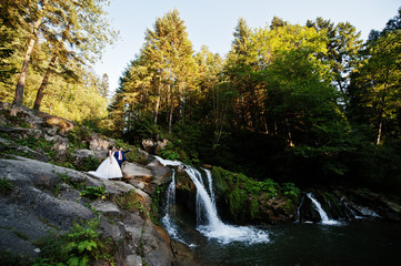 Lovely wedding couple against waterfall on sunset at Carpathian mountains.