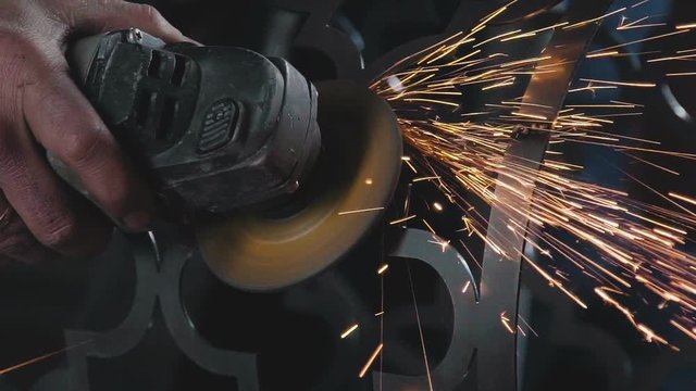 Decorative metalworking: the creation of an openwork decorative metal element. Back plan: the worker's arm holds an angle grinder with a circular cutting blade. The power tool is in operation.