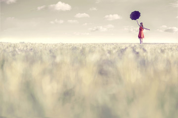 Surreal woman dressed in red walks with her umbrella in the middle of nature