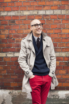 Portrait of smiling man standing with hands in pockets against brick wall