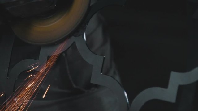Decorative metalworking: the creation of an openwork decorative metal element. Sparks when cutting and grinding a metal product. Process of creating a decorative metal product: forged openwork metal.