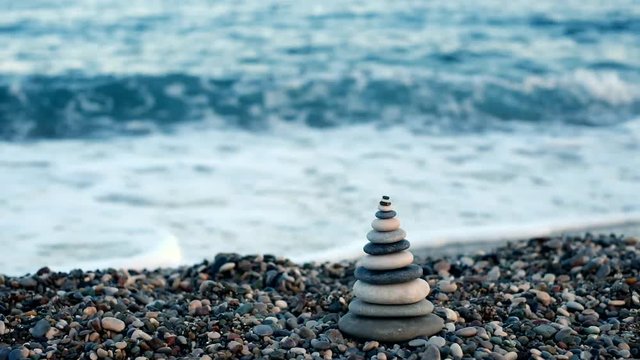 Closeup of pyramid made by sea stones on stony seashore at blurred blue sea water background. Beautiful nature landscape. Real time video footage