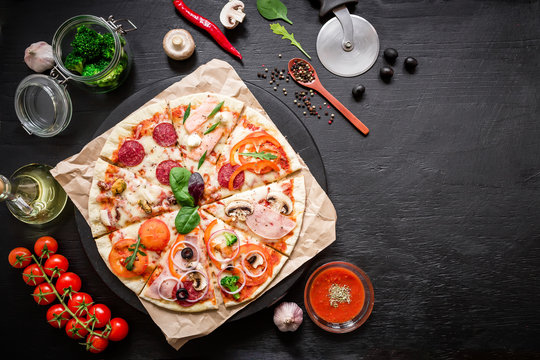 Food frame made of italian pizza with ingredients, vegetables and spices on dark background. Flat lay, top view.