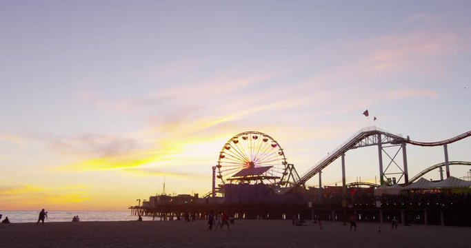People relaxing on the beach next to the Santa Monica Pier during sunset.