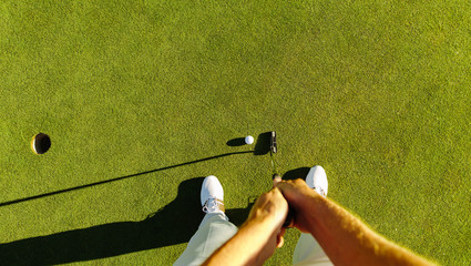 Golf player at the putting green hitting ball into a hole