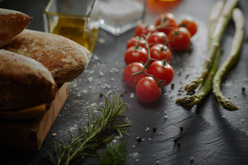 Cucina mediterranea, pomodorini, olio, sale, asparagi su fondo lavagna
