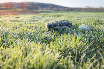 Baseball glove and ball on grass field in early morning dew at dawn