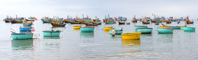 Fototapeta na wymiar Mui Ne, Vietnam - February 19th, 2017: Fishing village and traditional Vietnamese fishing boats with hundreds of boats moored in a line beautifully. This is the bay for boat storm in central Vietnam