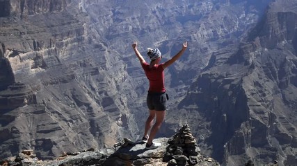 Young woman raising arms in victory standing on rock near canyon

