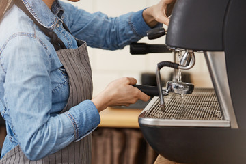 Closeup of female barista cleaning bottomless portafilter with steamer.