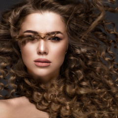 Fototapeta premium Beautiful brunette girl in move with a perfectly curly hair, and classic make-up. Beauty face. Picture taken in the studio on grey background.