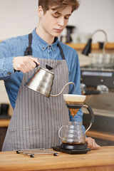 Male barista pouring water through grounds making pourover coffee.