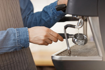 Male bartender in denim shirt and apron cleaning bottomless portafilter.