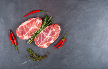 Two meat steaks, chili pepper and aromatic herbs on a dark background