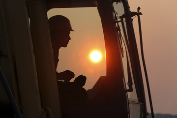 silhouette of an excavator driver in cabin on sunset