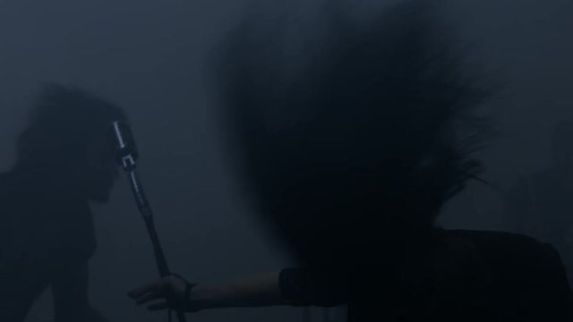Rock woman soloist shakes her head at rock concert. Rock soloist girl performs on stage. Rock girl silhouette. Metal band on scene. Close up metal girl singing