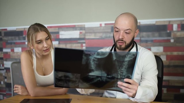 bald adult 30s doctor is showing x-rays to a patient and discuss it