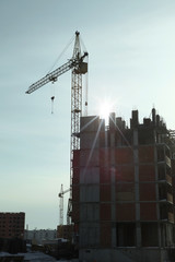 Under construction high-rise building with yellow construction crane in the sunlight