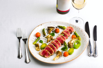 Salad of tuna and vegetables with a glass of wine and a bottle of wine on a white tablecloth, studio light