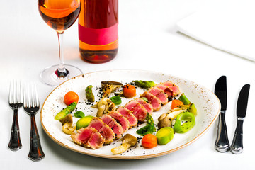 Salad of tuna and vegetables with a glass of wine and a bottle of wine on a white tablecloth, studio light