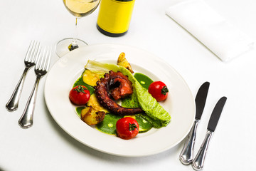 Seafood dish with fried octopus tentacles and vegetables with a bottle and a glass of wine on a white tablecloth background, studio light