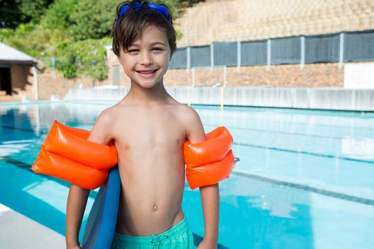 Smiling boy standing with kickboard and armband at poolside