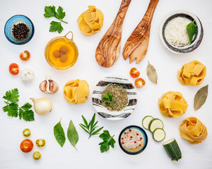 Italian foods concept and menu design. Dried fettuccine with wooden spatula and ingredients sweet basil ,tomato ,garlic ,parsley ,bay leaves ,pepper and zucchini on white wooden background flat lay.