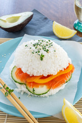 Sushi burger from rice, salmon, cucumber and pepper on a blue plate. Bright image of eating fast food.
