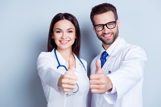 Happy medic workers. Portrait of two doctors in white coats and glasses showing thumb-up against white background