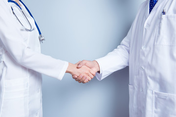 Deal! Concept of collaboration in medicine. Close up photo of two doctors' handshake on gray...