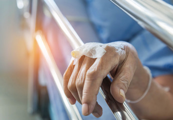Close up hand of elderly patient with intravenous catheter for injection plug in hand during lying in hospital ward room